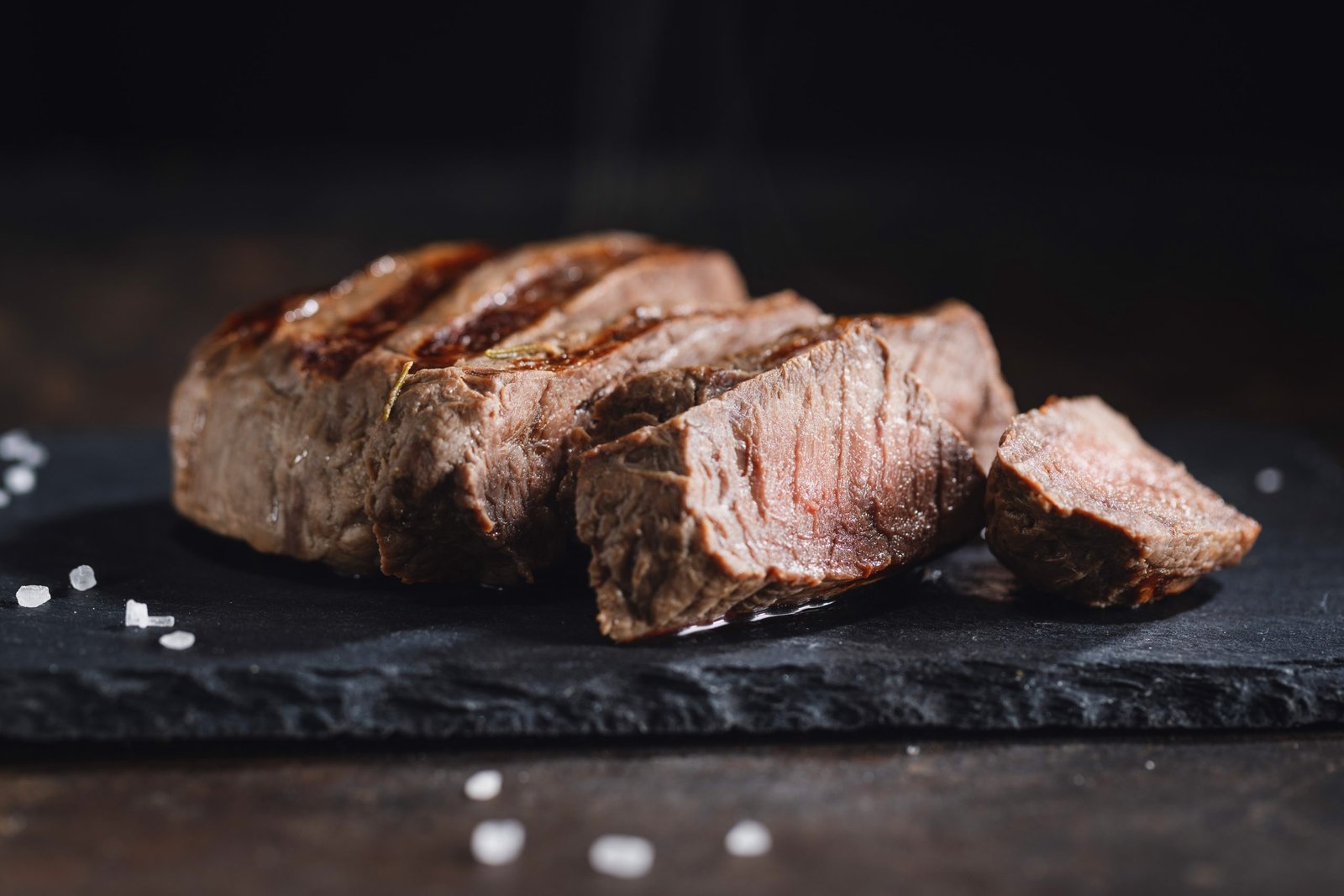 Grilled meat cut in slices on dark slate